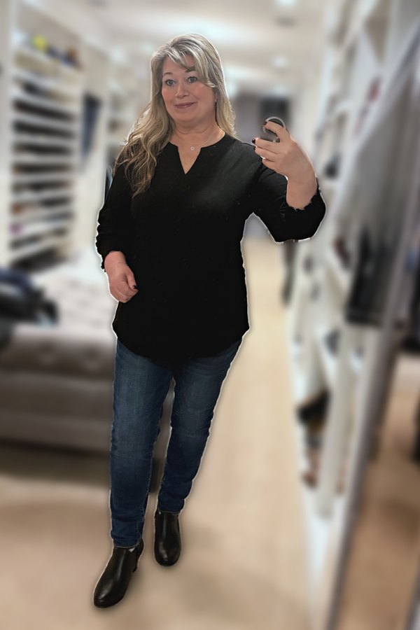 Mirror selfie of a woman wearing a black ruffle-cuff V-neck tunic, dark jeggings and black ankle boots
