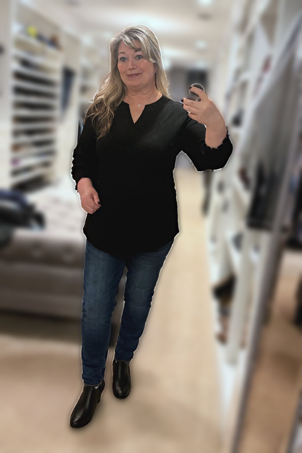 Mirror selfie of a woman wearing a black ruffle-cuff V-neck tunic, dark jeggings and black ankle boots