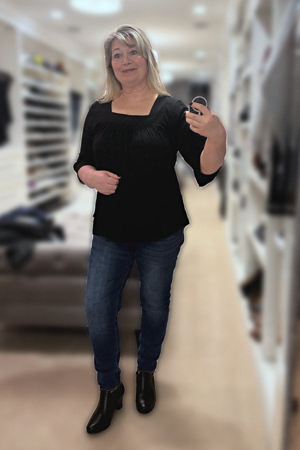 Mirror selfie of a woman wearing a black square-neck ruffle-sleeve top, dark jeggings and black ankle boots