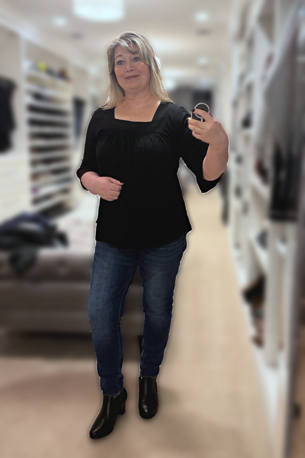 Mirror selfie of a woman wearing a black square-neck ruffle-sleeve top, dark jeggings and black ankle boots
