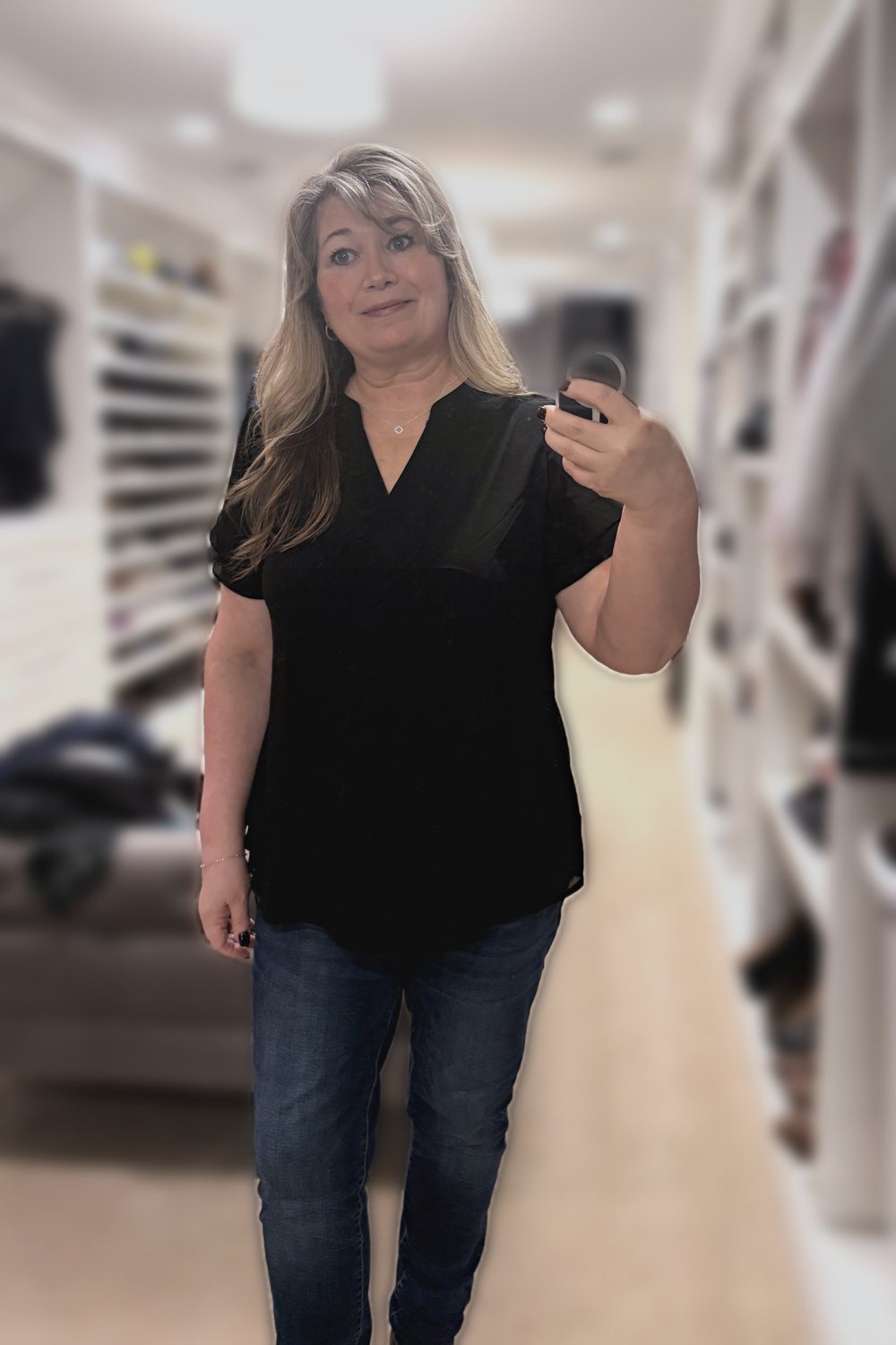 Mirror selfie of a woman wearing a black petal-sleeve V-neck top, dark jeggings, a dainty clover necklace and a silver bead bracelet