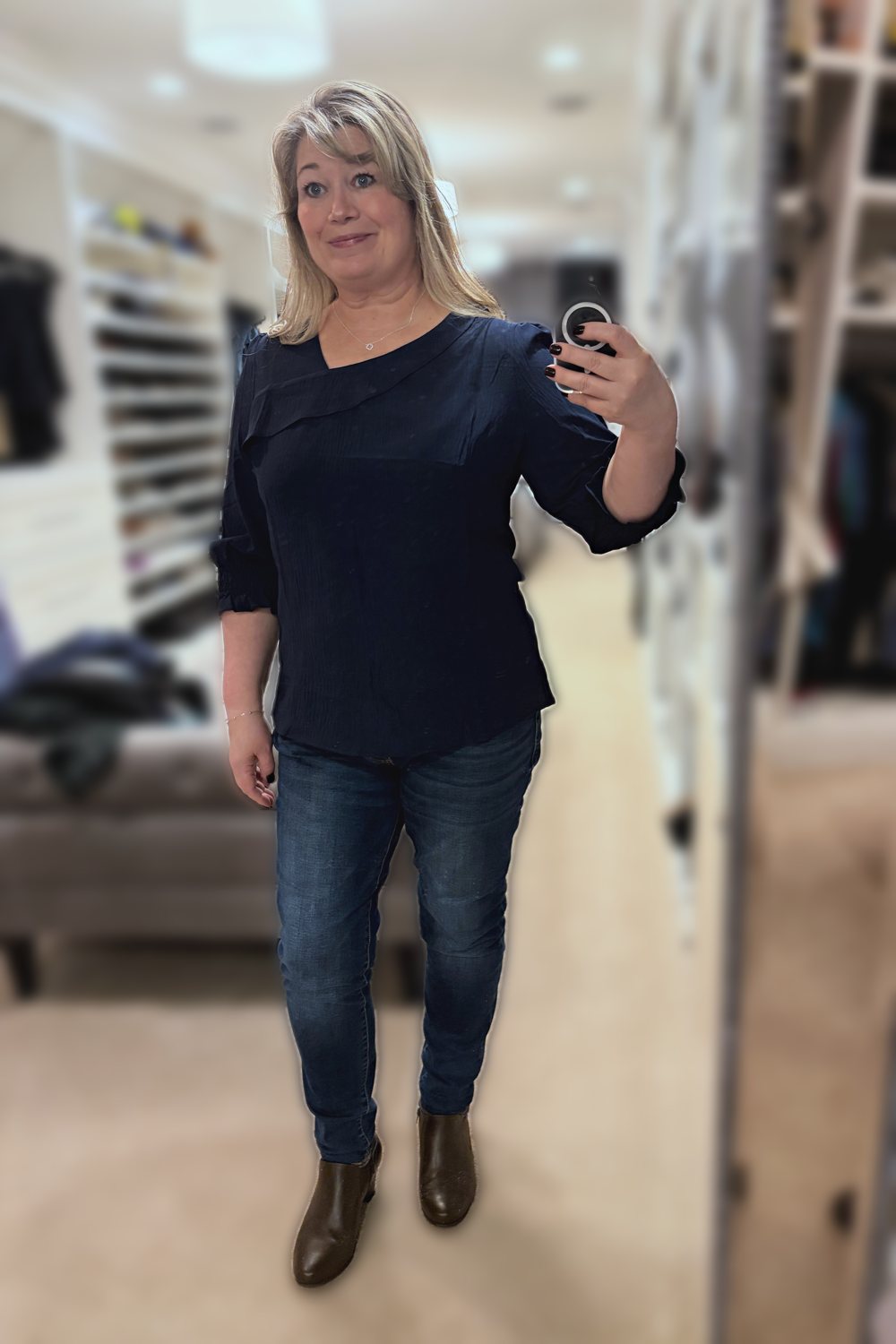 Mirror selfie of a woman wearing a navy smocked-cuff blouse, dark jeggings and brown ankle boots